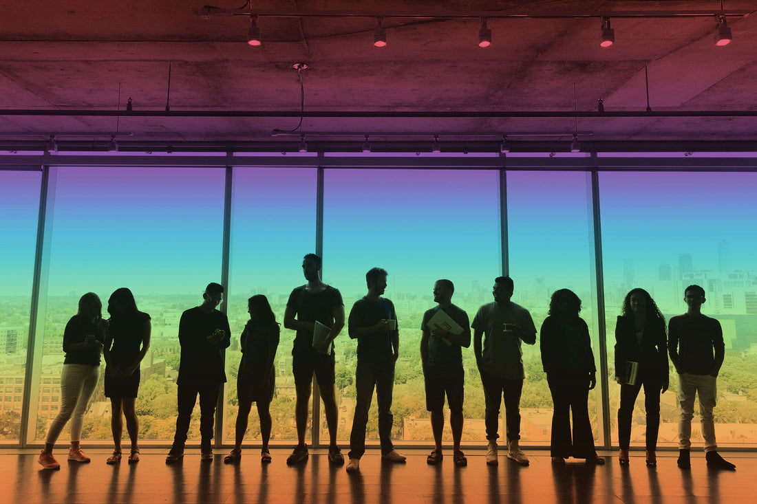 Silouette of a group of office workers standing in front of a window, overlaid with a rainbow-colored wash signifying neurodiversity.